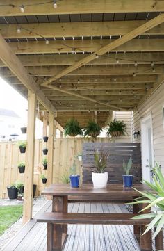 a wooden deck with potted plants and lights hanging from the pergolated roof