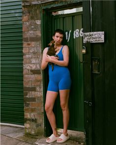 a woman holding a cat in her arms while standing next to a green door with graffiti on it