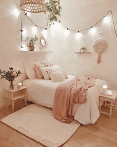 a bedroom with white walls and wooden flooring, lights strung from the ceiling over the bed