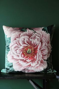 a pink flower on a green pillow sitting on top of a wooden shelf in front of a green wall