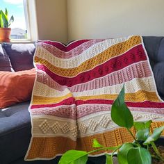 a crocheted blanket sitting on top of a couch next to a potted plant