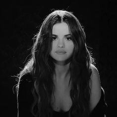 a black and white photo of a woman with long hair in front of a dark background