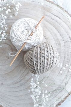 two balls of yarn sitting on top of a piece of wood next to knitting needles