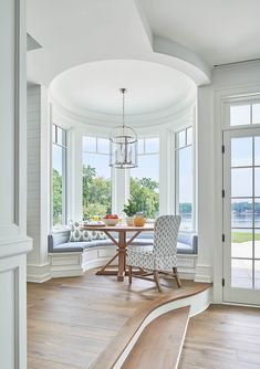 a dining room table and chairs in front of large windows with white trim on the walls