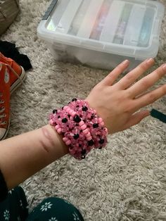 a person's hand with pink and black beads on it, next to a plastic container