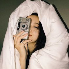 a woman under a blanket holding up a camera