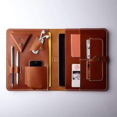 a brown leather case with pens, phone and other items in it on a white surface