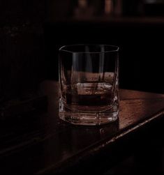 a glass sitting on top of a wooden table next to a window sill in a dark room