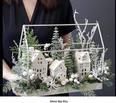 a woman is holding a christmas decoration with white houses and evergreens in the center