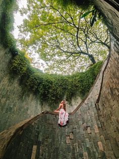 a woman sitting on top of a brick wall next to a tree filled with leaves