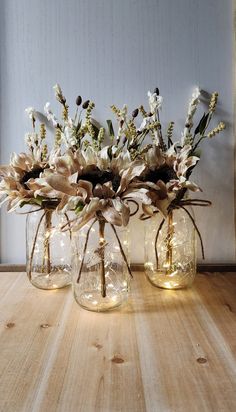 three glass vases filled with flowers on top of a wooden table