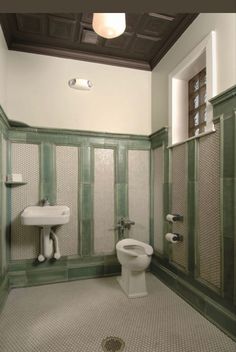 a bathroom with green and white tiles on the walls, two toilets and a sink