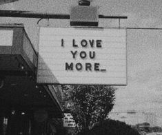 a sign that says i love you more hanging from the side of a building in black and white