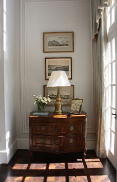 a room with a lamp, dresser and pictures on the wall in it's corner