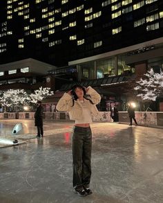 a woman is standing in an ice rink at night with her hands on her head