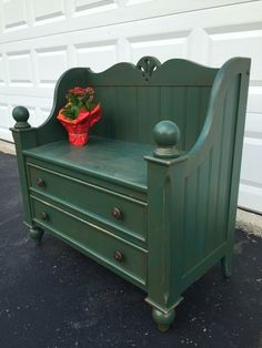 a green wooden bench sitting in front of a garage door with a potted plant on it