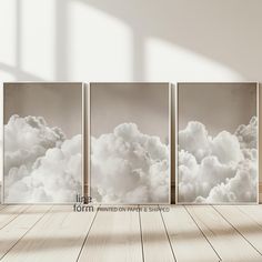 an empty room with three canvases on the wall and clouds in the sky above them