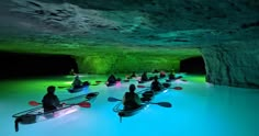 several people in kayaks paddle through the water inside a cave with green lights on it