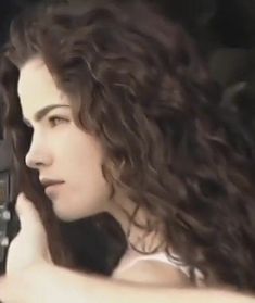 a woman holding a cell phone to her ear and looking off into the distance while sitting in a car