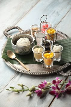 an assortment of desserts on a tray with spoons and flowers in the background