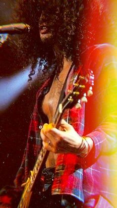 a man with long hair holding a guitar in front of a microphone and stage lights