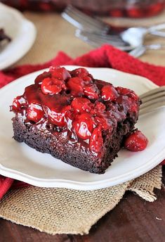 a piece of chocolate cake with cherries on it and a fork in the foreground