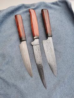 three knives sitting on top of a blue towel next to each other with wooden handles