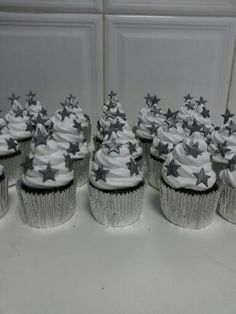 cupcakes with white frosting and silver stars on them are lined up in rows