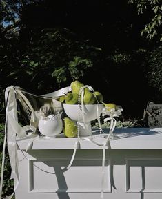 a white table topped with green apples covered in pearls and ribbons next to a tree