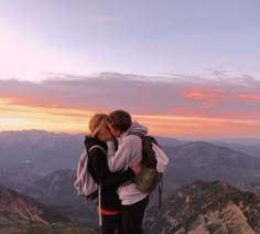 two people standing on top of a mountain kissing