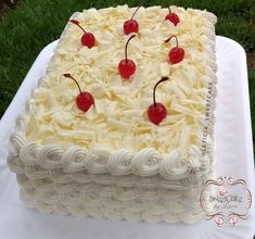 a square cake with white frosting and cherries on the top is sitting on a table