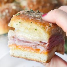 a hand holding a ham and cheese sandwich in front of other pastries on a plate