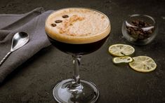 a drink in a glass next to some lemons and coffee beans on a table