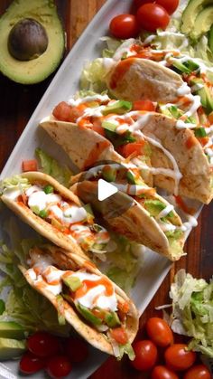 three tacos on a plate with lettuce, tomatoes and avocado