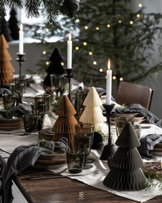 a dining room table set for christmas with candles and ornaments on the table, surrounded by pine trees