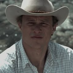 a man wearing a cowboy hat standing in front of some rocks and water with his eyes closed