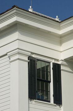 a white building with black shutters and a clock on it's front porch