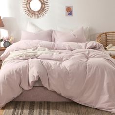 a bed with pink sheets and pillows in a room next to a wall mounted mirror