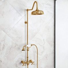 a gold shower head and handset in a white tiled bathroom with marble tiles on the wall