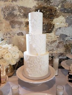 a three tiered white cake sitting on top of a table next to flowers and candles