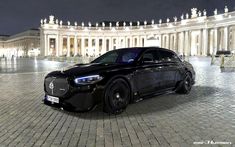 a black car parked in front of a white building at night with its lights on