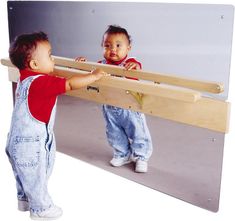 two toddlers playing with a large mirror in front of their face and one holding onto the wall