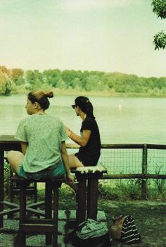 two women sitting at a picnic table near the water