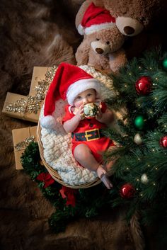 a baby wearing a santa hat and holding a pacifier in front of a christmas tree