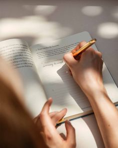 a person is writing on a book with a pen in their hand while holding a notebook