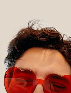 a close up of a person wearing red heart shaped sunglasses with hair blowing in the wind