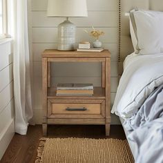 a nightstand with a lamp on top of it next to a bed in a bedroom