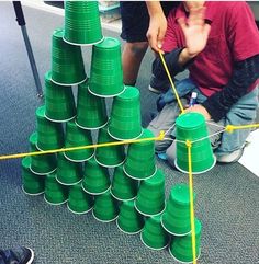 two boys are playing with green cups on the floor in front of a pile of them