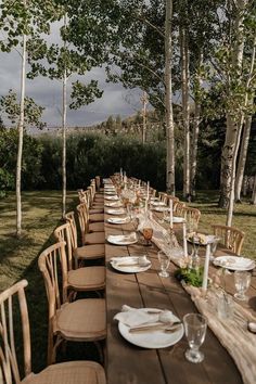 a long table set up with place settings for an outdoor dinner party in the woods