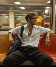 a man in white shirt and black pants sitting on a subway train with handbag